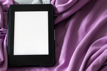 A modern black e-reader electronic book with a blank screen on a gray and purple bed. Mockup template tablet on microfiber bedding closeup
