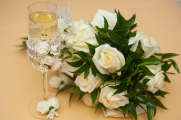 wedding bouquet of white roses with pearls on a pastel peach color. champagne glass decorated with beautiful lace, white roses flowers and pearl beads. wedding decoration with fresh flowers 