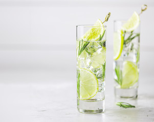 Refreshing lemon lime drink with ice cubes in glass goblets against a light gray background. Summer fresh lemon soda cocktail with rosemary, selective focus