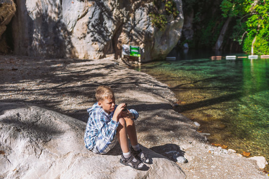 Young Kid Trying To Take Photoes Of Beautiful Scenic Sunny Landscape But It Is Hard To Do In Bright Sunlight. Boy Taking Good Look And Gazing At Screen Of Mobile Phone.