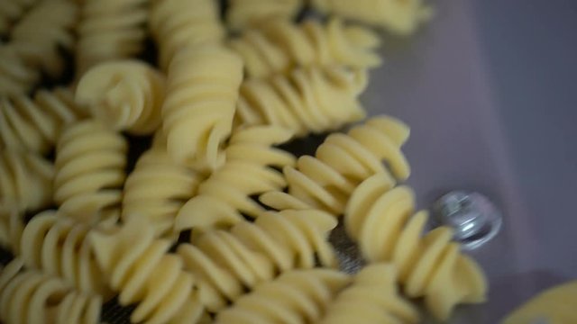 Close up shot of rotini scroodle macaroni fusilli short pasta passing on a conveyor belt machinery to prepare pasta in Italy.