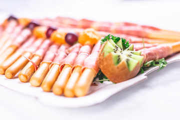 Close up of bread sticks grissini with prosciutto ham served on table.