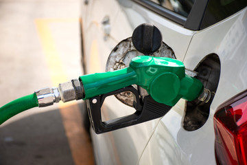 White car refueling at gas station with green fuel nozzle.