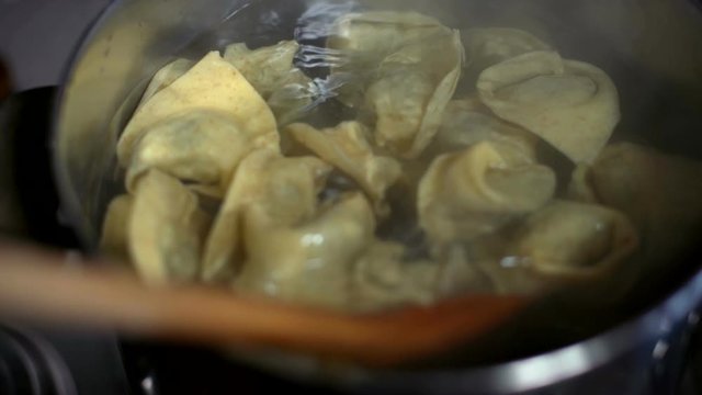 Stirring tortellini pasta with a wooden spoon in a pot with boiling water.
