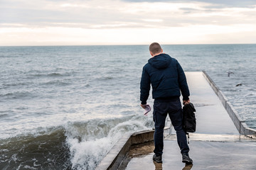 A lone traveler stands on a pier by the sea. Figure of a man on the background of the sea.