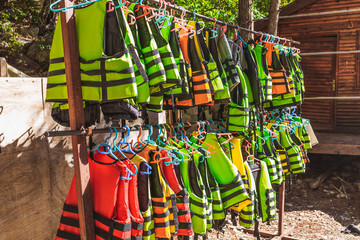 Many colorful life vests of yellow, orange, green and red colors hanging outdoor on sunny summer...