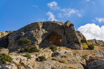 Fototapeta na wymiar Cape Alchak on southern coast of Crimea on outskirts of resort town of Sudak. Fabulous view of big mountain with Aeolian harp grotto on Alchak-Kaya trail. Close-up of huge stones and natural boulders