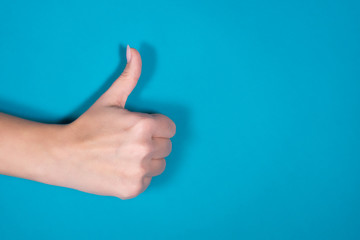 Closeup top view photography of beautiful manicured female hand making like and approval gesture holding big thumb up isolated on bright blue background.