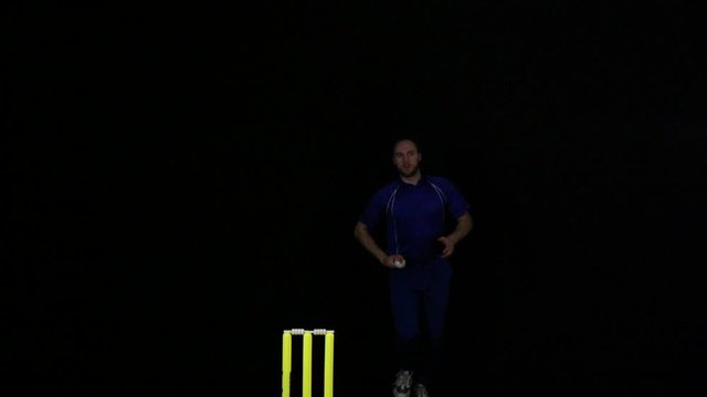 Cricket Bowler bowling the ball in a game of the sport- Black background. Dressed in Blue. T20 Cricket