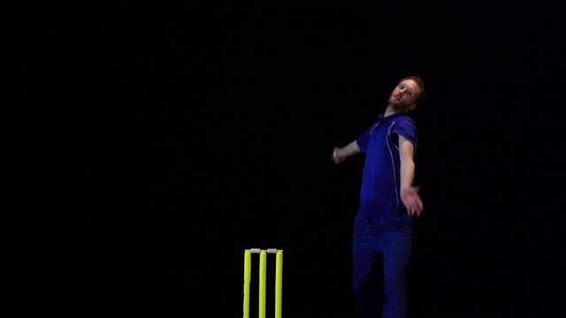 Cricket Bowler bowling the ball in a game of the sport- Black background. Dressed in Blue. T20 Cricket