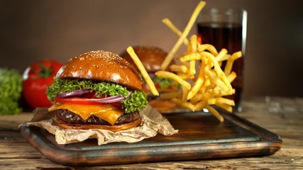 Super Slow Motion Shot of Fast Food Concept. Falling French Fries on Wooden Cutting Board next to the Fresh Hamburger at 1000fps.