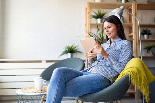 Beautiful young woman relaxing at home with digital tablet