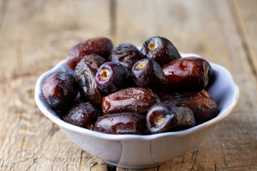 Beautiful juicy date with water drops. Fresh dates plucked from a tree in a plate. Dried dates on a wooden table, still life. Vegetarian food. Sweet snack. Large sweet dates close-up. Useful sweets fo