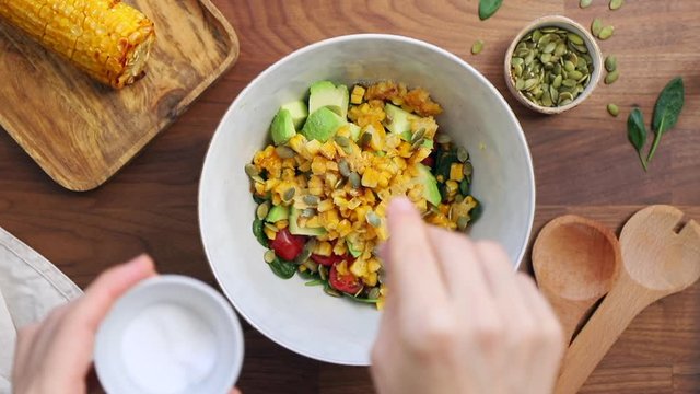 Adding salt to a bowl. Healthy eating concept, making healthy summer salad with vegetables. View from above.
