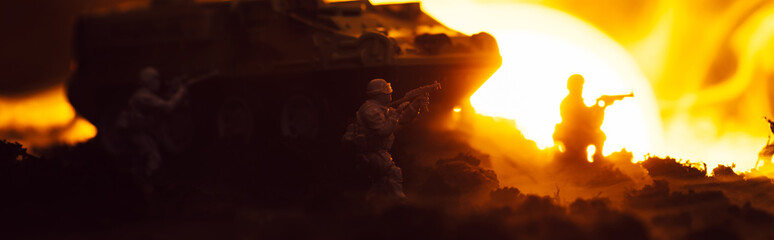 Battle scene with toy warriors, tank and fire with sunset at background, panoramic shot
