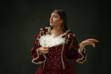 Portrait of medieval young woman in red vintage clothing posing with fluffy fur on dark background....