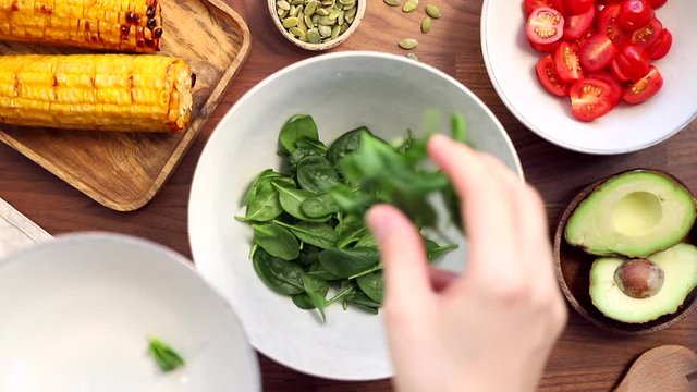 Adding fresh spinach to a bowl. Healthy eating concept, making healthy summer salad with vegetables. View from above.