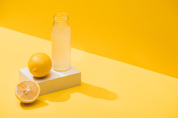 fresh juice in bottle near lemons and white cube on yellow background