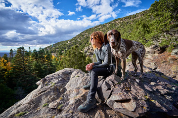 a young woman and her dog hiking to the top of a mountain