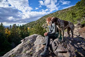a young woman and her dog hiking to the top of a mountain