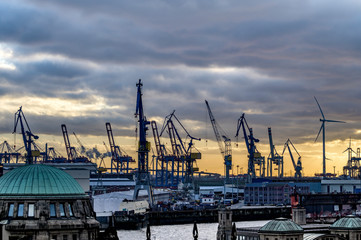 Obraz premium Der Hamburger Hafen am Abend mit Hafenkränen und Windrädern im Gegenlicht