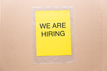 We are hiring printed on yellow paper on transparent plastic bag with cardboard background. Hiring board employment concept