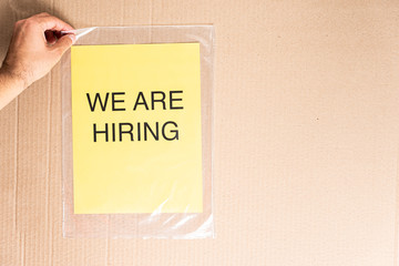 We are hiring text on yellow paper sheet on transparent bag and cardboard background. Hiring terms contract employment concept