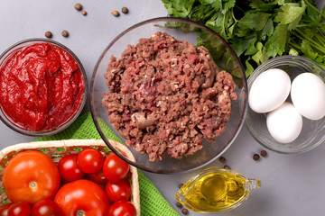 Minced meat with tomatoes, eggs, parsley and pepper on a gray background. Forcemeat. Top view.