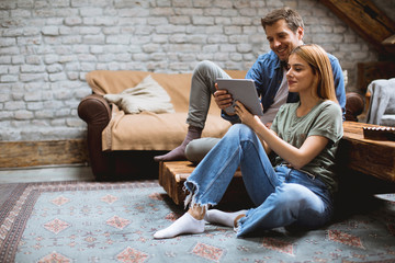 Happy couple using digital tablet while sitting  together oh the floor