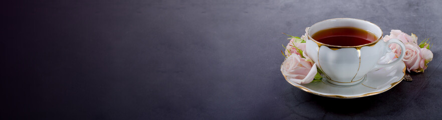 Tea time banner with vintage white porcelain tea cup, gentle pink roses on a dark gray background.
