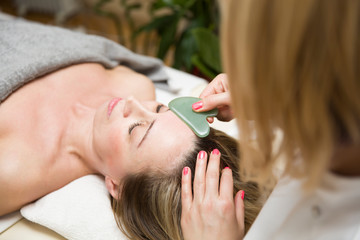 Woman having an gua sha facial massage with natural jade stone massager