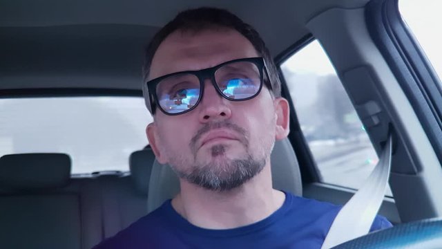 White man with glasses talking at steering wheel on old black small cellular phone