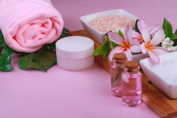 Obraz na płótnie Canvas Spa composition with bowls with rock white and pink salt and flowers, towel, cream and lotion on pinkk background. Body scrub and massage treatment