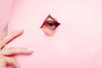 cropped view of girl with pink makeup looking through torn paper