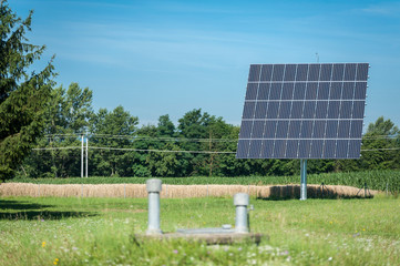 Solaranlage steht in Wiese, dahinter Eisenbahn Stromleitung und Wald