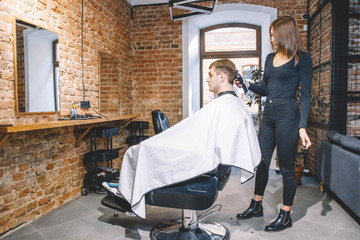 Beautiful woman hairdresser makes a haircut the client's head with a electric trimmer in barber shop. Advertising and barber shop concept. Place for text or advertising