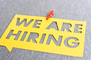 "WE ARE HIRING". Yellow speech bubble banner on blank gray textured background. Job search and employment concept