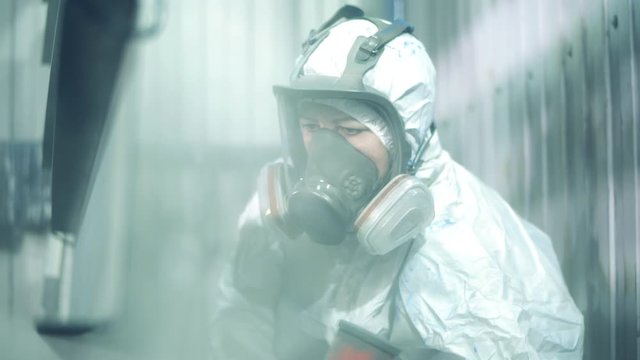 Close up of female worker's face in safety wear during painting metal. Industrial painting process at painting factory facility.
