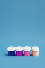 Colorful vibrant cans of gouache paint isolated on color blue background. Painting background. A set of acrylic paints in jars for the artist. Copy space. The concept of creativity and minimalism