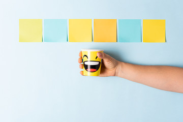 Hand showing a happy paper cup on blue background with multicolor paper notes. Happy work, award,...