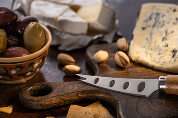 selective focus of dorblu and brie cheese with olives and pistachios near knife