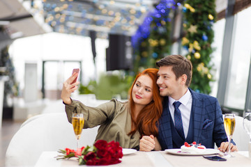 beautiful caucasian lady take selfie with handsome man in restaurant, couple on a date. young man and woman have romantic evening, they celebrate anniversary or birthday, wearing party clothes