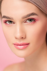 Fototapeta premium attractive girl with pink makeup looking at camera, isolated on pink