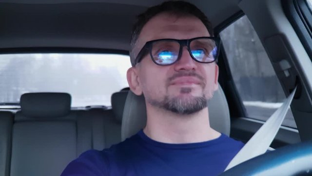 Caucasian man drives passenger car and smiles. Very strong reflection in his glasses