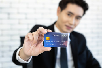 Asian handsome young businessman Abstract blur with focus on show holding a credit card lying sit on the table In the office room white wall background.