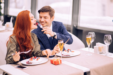 couple sit in restaurant together. couple celebrating anniversary, spend romantic day in rich restaurant. careful handsome guy in elegant stylish tux treats his girlfriend with tasty sweet dessert