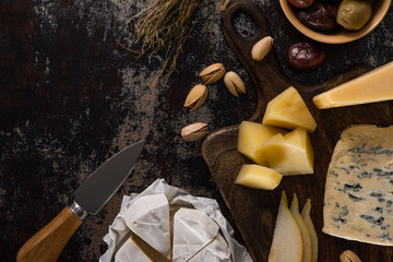 top view of cheese platter with pistachios, sliced pear, olives and knife on weathered surface