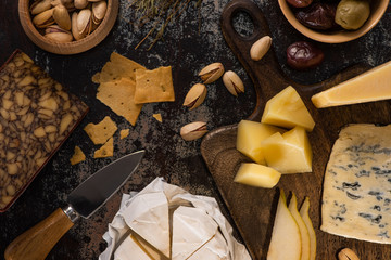 top view of cheese platter with pistachios, sliced pear, olives and crackers on weathered surface
