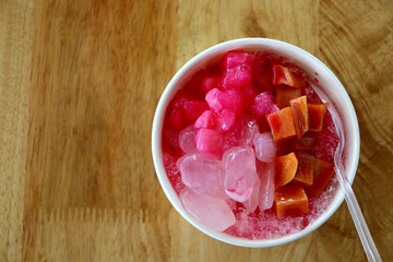 Top view of shaved ice with milk and topping in cup on wooden table background. Summer concept.