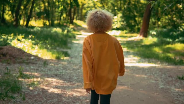 back view woman with blond curly hair walking in forest slow motion